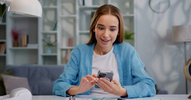 Kapalı kapılar ardında sevinçli bir kız, iyi haberler okuyor, cep telefonundaki başarının tadını çıkarıyor. Modern bir dairede zaferi kutlayan sürpriz bir bayan.