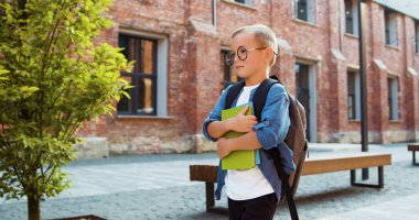 Okuldan sonra elinde kitaplarla dolaşan sırt çantalı küçük mutlu bir çocuk. Macera öğrenimi, yürüyüş bilgisi, çocuk öğrenci. Anaokulunda. Okula geri dön..