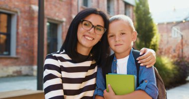 Kapatın. Ön manzara. Sevgi dolu genç bir anne ve sevimli küçük çocuklar kameraya bakıyor mutlu bir aile okul binasının yanında poz veriyor. Mutlu aile kavramı.