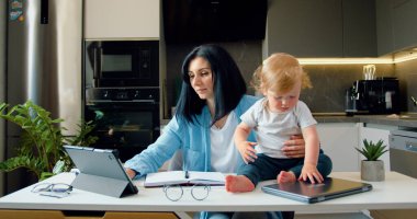 Anne, küçük çocukları oynarken ve onu rahatsız ederken dizüstü bilgisayarla çalışmaya çalışıyor. Uzaktan çalışma ve evde çocuklarla eğlenme. Serbest çalışıyorum, oğlumla evde çalışıyorum..