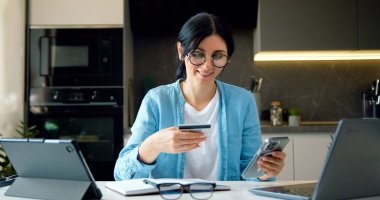 İş kadını internet üzerinden alışveriş yapmak için banka kredi kartı numarasına giriyor. Kredi kartı ve telefonuyla evden alışveriş yapan esmer bir kadın internet bankacılığı..