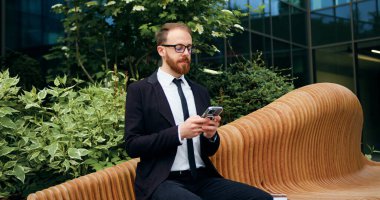 Genç işadamı iş bölgesinde bankta otururken verileri analiz ediyor. Yakışıklı erkek e-postaları kontrol ediyor, internette sohbet ediyor, bir müşteriyle mesajlaşıyor, sosyal medyada geziniyor..