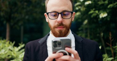 Kapatın. Gözlüklü neşeli adam dışarıda bankta oturmuş akıllı telefon kullanıyor. Ofis binasının yanındaki bankta dinlenen kendine güvenen sakallı erkek cep telefonuna mesaj atıyor..