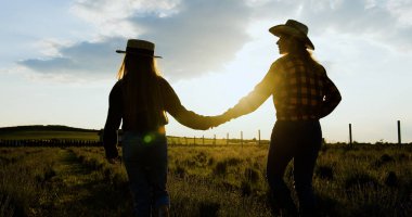 Anne, şapkalı kız gün batımında el ele yürüyorlar. Kadın çocuğu elleriyle tutuyor. Aktif yaşam tarzı konsepti. Mutlu aile kavramı.