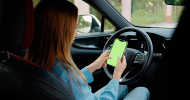 Genç kadın elleri modern araba krom anahtar akıllı telefon teknolojisinde dikey yeşil ekranlı akıllı telefon kullanıyor..