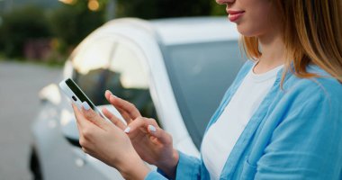 Yakın plan. Genç hippi kadın gün batımında park arabasının yanında telefonla yazı yazıyor. Dışarıda cep telefonu tutan bir kız, şehir geçmişi. Sosyal ağlar, haber sohbetleri