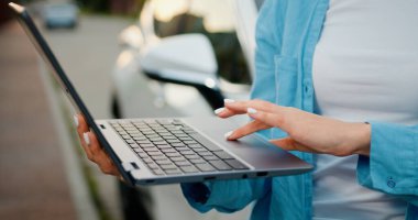 Kapatın. Sokakta dikilirken dizüstü bilgisayar kullanan beyaz kadın elleri. Otoparkın yakınındaki dizüstü bilgisayarda kadın dinlenmesi ve mesajlaşması. Açık havada..