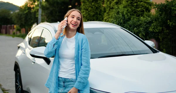 Beyaz, kendine güvenen bir kadın şehirde caddede duruyor ve dışarıda cep telefonuyla konuşuyor. Park arabasının yanındaki sokakta akıllı telefon kullanan genç bir kadın..