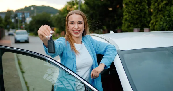 Portrait of young woman standing near car holds keys with delighted and show keys wants to buy new automobile in car. Attractive girl holding a key from her new car, smiling and singing.