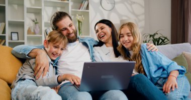 Gülümseyen çocuklar anneleri ve babaları birlikte vakit geçiriyorlar internette eğleniyorlar dizüstü bilgisayar kullanarak çizgi film izliyorlar. Aile, gülümseyen ailelerle film izliyor..