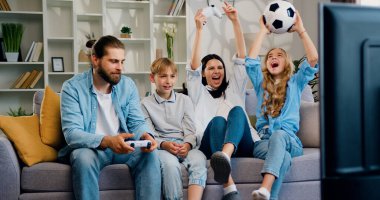 Mutlu bir aile evde kanepede oturup video oyunu oynuyor. Eğlence ve modern yaşam tarzı konsepti. Ebeveynler ve çocuklar evlerinde video oyunu oynuyorlar..
