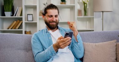 Genç adam cep telefonuna bakıyor ve iyi haberler okuyor. Kazananın ya da kazananın heyecanını hissediyor. Finansal hisse senedi sporları bahsi..