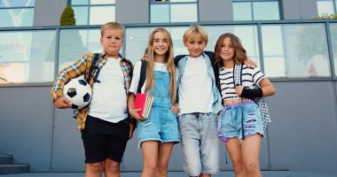 Sırt çantaları ve defterleriyle kameraya bakıp gülümseyen mutlu çocukların portresi. Okul binasının dışındaki kameraya gülümseyen çok ırklı öğrenciler..