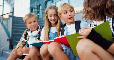 Bir grup özenli öğrenci modern okulun arka planında çember çizerek oturuyorlar ve açık hava dersleri sırasında notlar alıyorlar. Takım çalışması, eğitim ve yeni yaklaşımlar kavramı