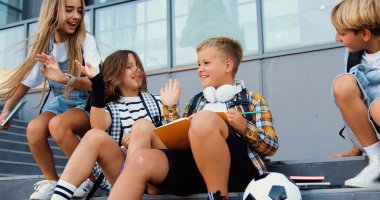 Çeşitli öğrenciler ilkokul binasını terk ediyor. Mutlu çocuklar dışarıda gülümseyerek konuşuyor. Sırt çantalı neşeli öğrencilerden oluşan bir grup merdivenlerde bir arkadaşının yanına oturup onu selamlıyor..