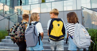 Dikiz aynası. İyi görünümlü okul çocukları sırt çantalarıyla sınıfa gitmek için merdivenleri tırmanırlar. Erkek ve kız lise öğrencileri okuldan sonra eğleniyorlar. Gülüyorlar ve eğleniyorlar..