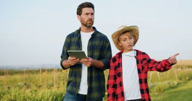 Tarla işçisi ve şapkalı genç bir adam ve tabletli çocuk gün batımında hasatçıların hasadını kombine ederek olgunlaşmış buğday topluyorlar. İşçi, buğday hasadını not tahtasıyla inceliyor. Buğday üretimi