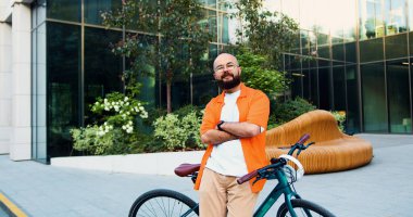 Kameraya bakan turuncu gömlekli yakışıklı genç adamın portresi. Yakışıklı, güler yüzlü, sakallı, sakallı, büyük şehir inşaatının yanında oturan..