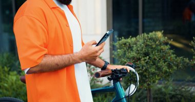Ofis merkezinde bisikletle yürürken akıllı telefon tutan erkek elleri. Şehre çevre nakli. Bisiklet sürerken sohbet etmek. Modern yaşam tarzı, bağlantı. Meşgul insanlar için modern aletler.