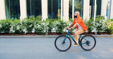 Klasik bisiklete binen şık bir hippi. Beyaz adam, şık günlük kıyafetli. Şehir duvarında bisiklet sürüyor. Sabah ofise giderken..