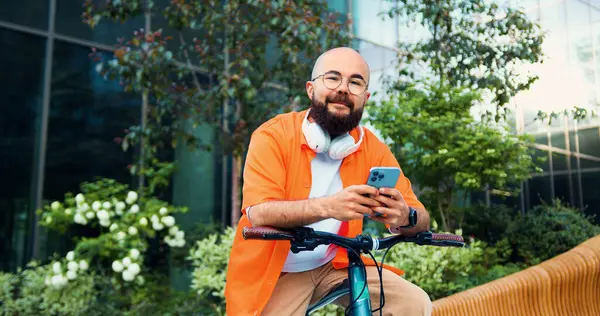 Kameraya bakan turuncu gömlekli yakışıklı genç adamın portresi. Yakışıklı, güler yüzlü, sakallı, sakallı, büyük şehir inşaatının yanında oturan..