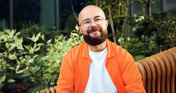 Gündelik kıyafetler giyen genç yakışıklı adam mutlu gülümsüyor. Gözlüklü neşeli adamın yakın portresi yaz parkında dışarıda oturan kameraya bakıyor..