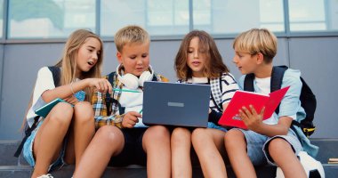 Group of school Children friends sitting together in school building downstairs talking and discussing education and studying uses book and laptop, outdoors. Concept of teenager students lifestyle clipart