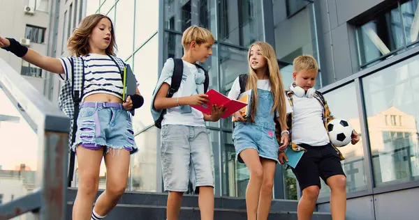 Group of four young attractive caucasian students walking together down the stairs in college campus talking and laughing with joy. Education and school children life concept