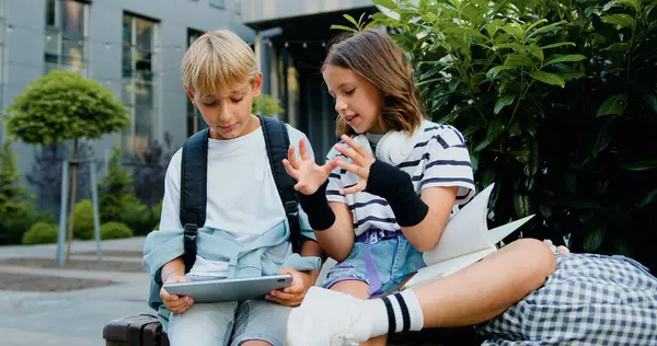 İki çocuk okuldan sonra dışarıda dinlenirken dijital masa tableti kullanıyor. Çocuklar ve alet konsepti