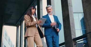 İki iş adamı, resmi takım elbiseli bir adam ve bir kadın işten sonra modern bir ofis binasının merdivenlerinden aşağı iniyorlar, sohbet ediyorlar. Kadın dijital tablet kullanırken, erkek dizüstü bilgisayar taşıyor. Yavaş çekim