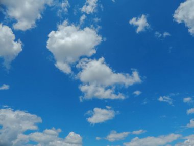 Pofuduk beyaz bulutlarla dolu çarpıcı bir mavi gökyüzü manzarası, arka plan veya seyahat broşürleri için idealdir. Güneş bulutların arasından parlıyor, resim gibi bir sahne yaratıyor..