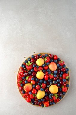 Gri arka planda bir tabakta çeşitli bahçe meyvelerinin karışımı.