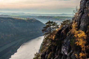 Su, yüksek dağlar ve yemyeşil ağaçlar tarafından kucaklanan bir vadiden akar ve açık gökyüzünün altında çarpıcı bir doğal manzara yaratır.