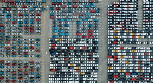 Aerial view of new cars stock at factory parking lot. Above view cars parked in a row. Automotive industry. Logistics business. Import or export new cars at warehouse. Big parking lot at port terminal