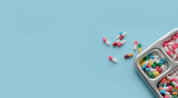 Above view of Colorful antibiotic capsule pills on a tray and blue background. Antibiotic drug resistance. Antimicrobial drugs. Prescription drugs. Pharmaceutical industry. Health care and medicine.