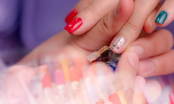 Woman receiving fingernail manicure service at nail salon. Beautician painting nails at nail and spa salon. Focused on white and glitter nail polish at nail salon with blur foreground of fake nails.