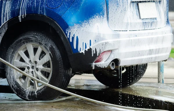 Blue car wash with white soap foam. Auto care business. Car cleaning and shining before waxing service. Vehicle cleaning service with antiseptic and disinfectant. Car washing service at car care shop.