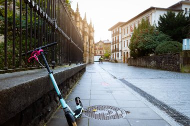 Elektrikli scooter Avrupa 'da caddenin yanındaki beton duvara yaslanıyor. Eski şehir yolunda eko taşıma. Şehir yaşam tarzı. Geleceğin ulaşımı. Sürdürülebilir yaşam tarzı. Tarihi yapı mimarisi.