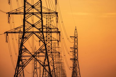 Yüksek voltajlı elektrik iletim kulesi. Elektrik direğindeki yüksek voltajlı elektrik hatları günbatımı gökyüzüne karşı. Elektrik altyapısı. Enerji krizi. Elektrik dağıtımı. Enerji dağılımı.