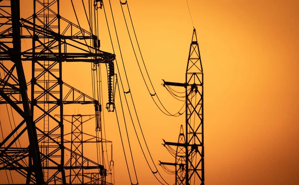 Yüksek voltajlı elektrik iletim kulesi. Elektrik direğindeki yüksek voltajlı elektrik hatları günbatımı gökyüzüne karşı. Elektrik altyapısı. Enerji krizi. Elektrik dağıtımı. Enerji dağılımı.