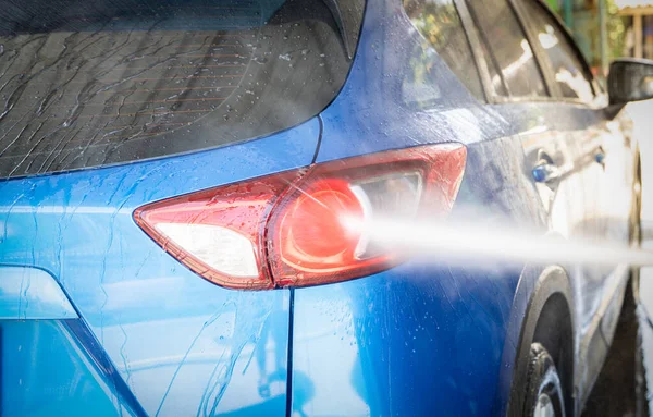 Car washing with high pressure water spray. Car cleaning. Auto care service concept. Vehicle cleaning. High pressure water spraying on tail light of blue car. Manual car wash with high pressure water.
