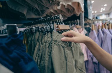 Giysi mağazasından yeşil şort alan bir kadın. Kıyafet seçen kadın. Elbise mağazasında askıda asılı duran şortlar. Alışveriş merkezindeki moda mağazası. Giysiler elbise dükkanında askılarda..