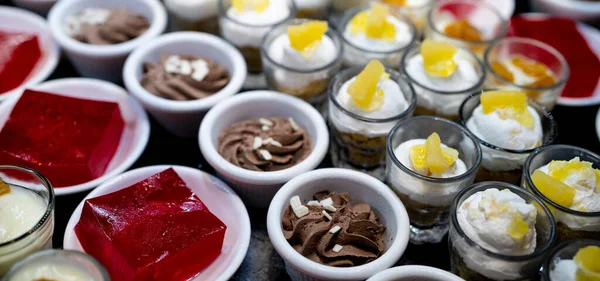 Dessert buffet catering concept. Selective focus dessert on buffet counter. Dessert in plate, cup, and glass on table at restaurant for lunch buffet. Sweet food. Red jelly agar, chocolate mousse.