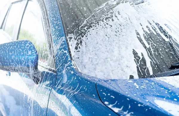 Blue car wash with white soap foam. Auto care business. Car cleaning service. Vehicle cleaning service. Foam wash car detailing. The windshield of blue luxury SUV car is covered with white foam.