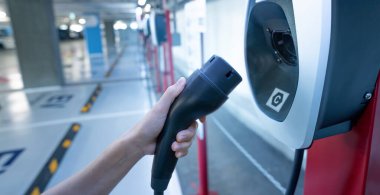 Hand holding electric charger at an electric vehicle charging station. Commercial EV car charging point for charge EV battery. Electric vehicle charging station at basement car parking lot of the mall