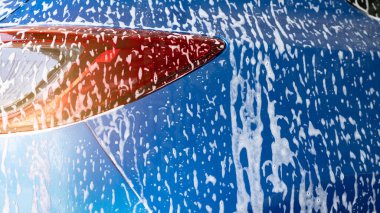 Beyaz sabun köpüğüyle mavi araba yıkama ve profesyonel oto bakım servisi. Araba temizleme servisi konsepti. Araç temizleme servisi. Köpük yıkama araba temizliği. Mavi lüks SUV arabası beyaz köpükle kaplıdır..