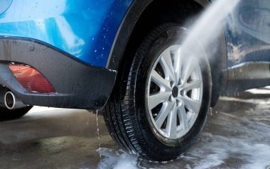 Yüksek basınçlı su spreyiyle araba yıkama. Araba temizliği. Oto bakım hizmeti konsepti. Araç temizliği. Araba tekerleği ve lastiğine yüksek basınçlı su püskürtülüyor. Yüksek basınçlı suyla elle oto yıkama..