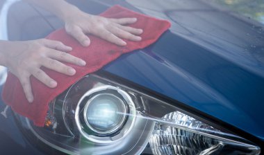 Araba yıkama servisi. Kırmızı mikrofiber bez tutan ve mavi arabanın farlarını parlatan bir adam. Oto bakım servisi konsepti. Lüks arabaları temizleyen ve temizleyen adam. Lüks arabadan temiz su damlıyor..