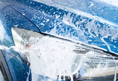 Beyaz sabun köpüğüyle mavi araba yıkama. Oto bakım işi. Araba temizleme servisi. Araç temizleme servisi. Köpük yıkama araba temizliği. Mavi lüks SUV arabasının far ışığı beyaz köpükle kaplıdır..