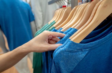 Kadın giysi mağazasında alışveriş gömleği. Kıyafet seçen kadın. Elbise mağazasında askıda asılı tişört. Alışveriş merkezindeki moda mağazası. Bir giyim mağazasında elbise askısı..